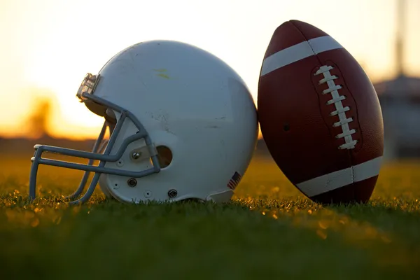 Футбол и шлем на поле на закате Стоковое Изображение