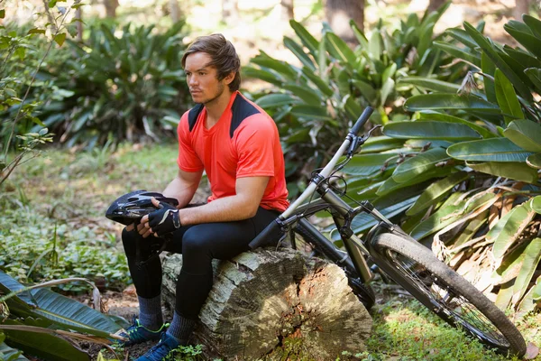 Измученный мужской горный байкер расслабляющий на стволе дерева в лесу — стоковое фото